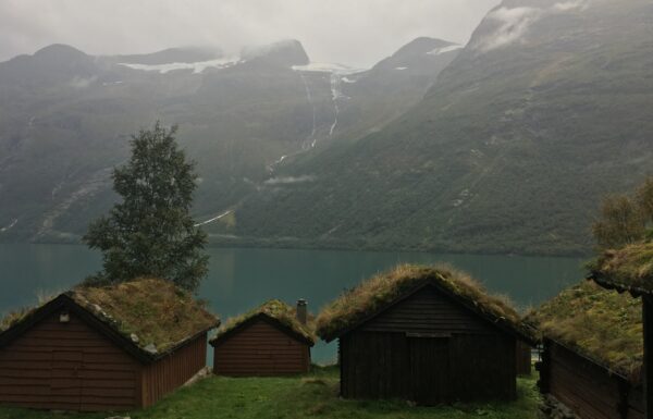 spowity mgłą krajobraz, na pierwszym planie drewniane domki z dachami pokrytymi trawą, w tle jezioro i wznoszące się nad nim szczyty