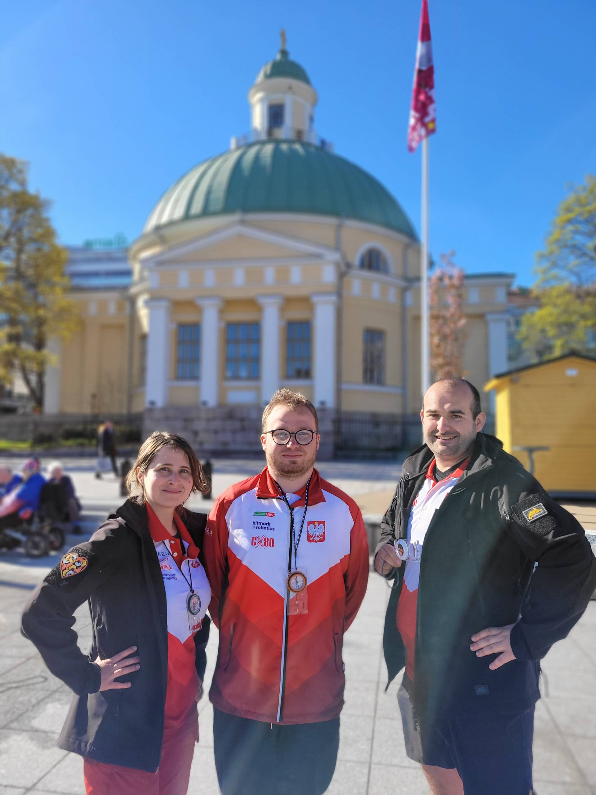 troje uczestników zawodów w orientacji precyzyjnej, kobieta i dwóch mężczyzn, stoją na tle budynku