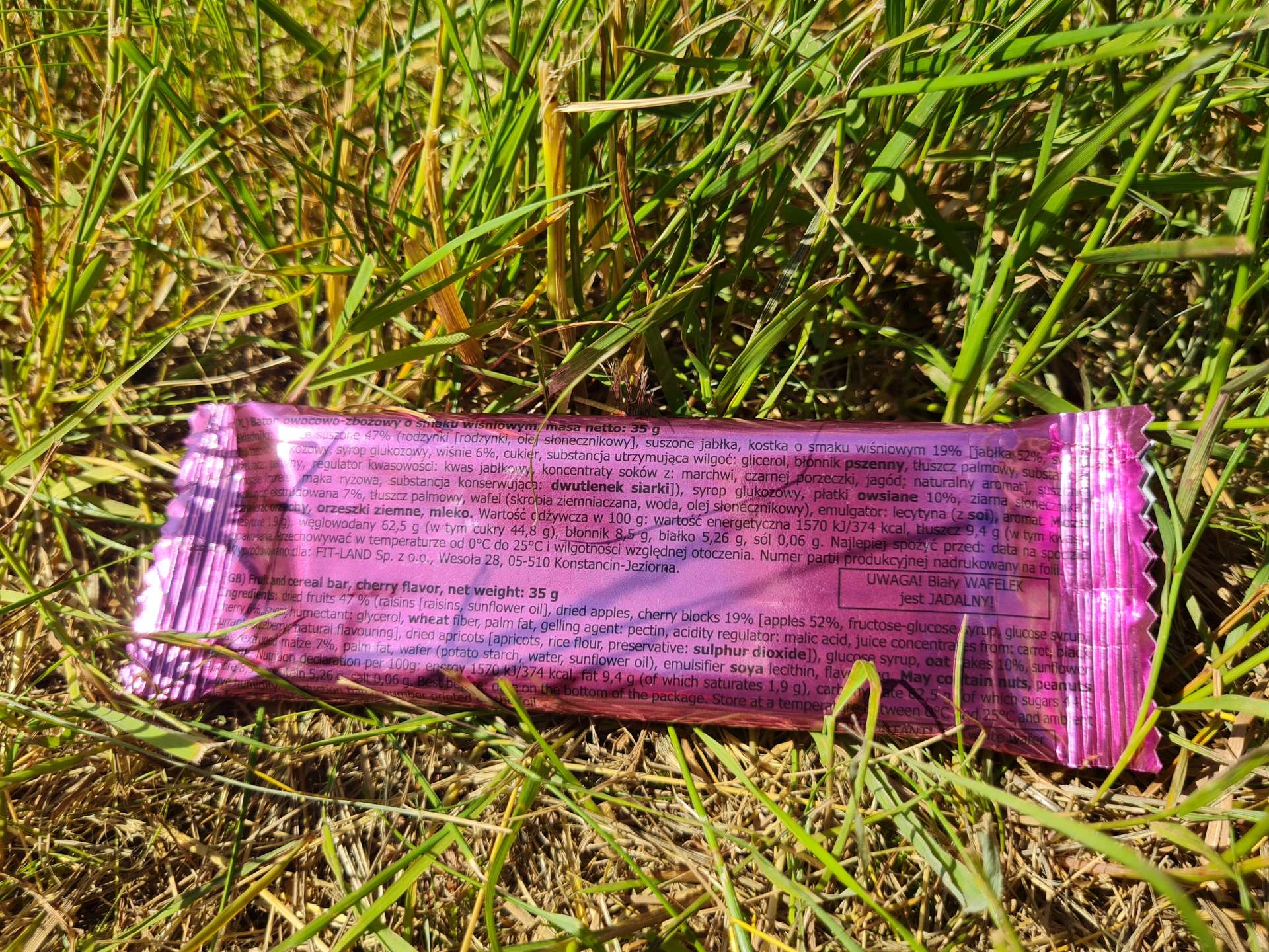 baton owocowo-zbożowy w różowym opakowaniu położony na trawniku
