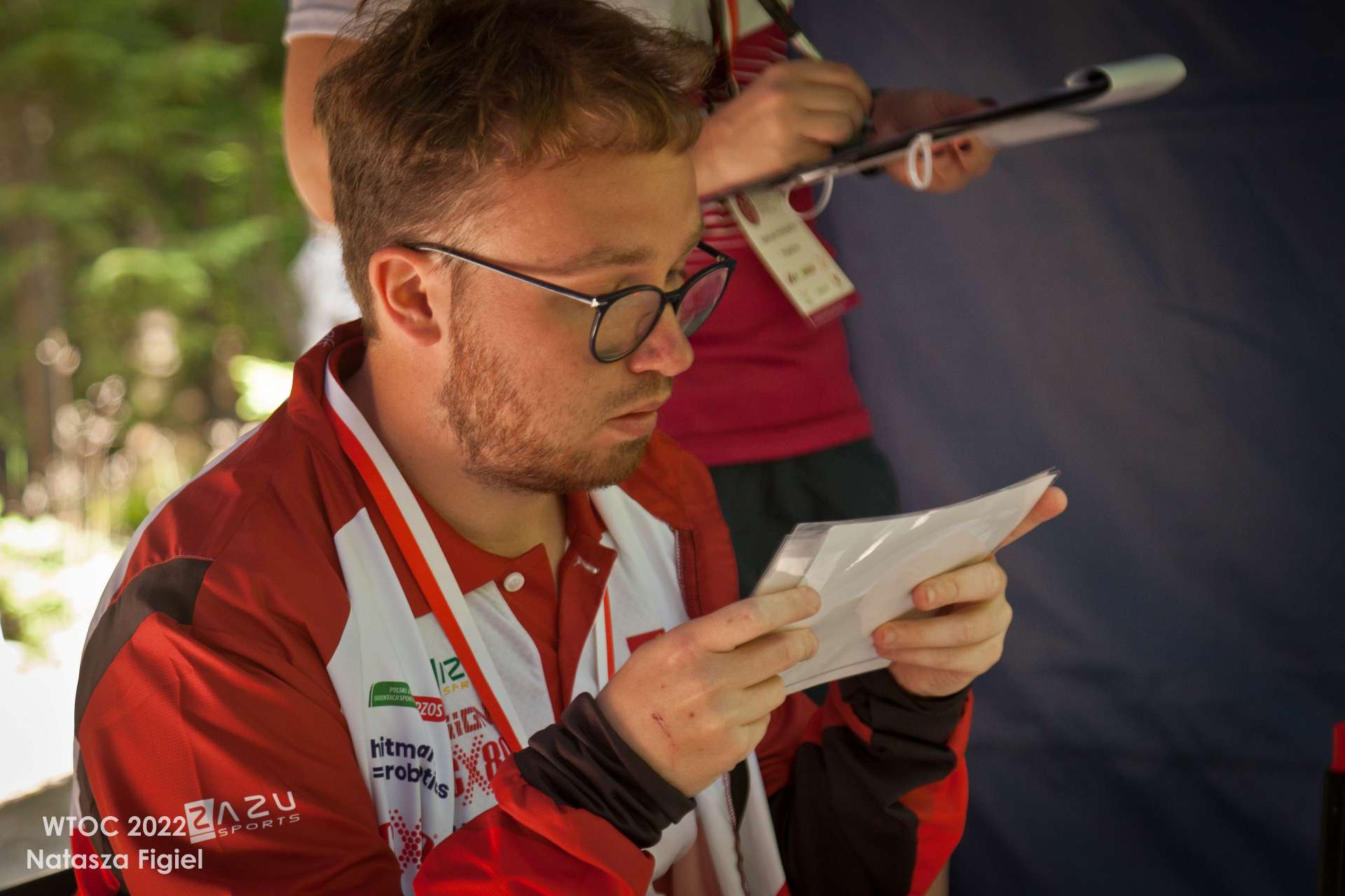 mężczyzna w okularach trzyma w dwóch rękach kartkę, której uważnie się przygląda