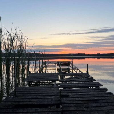 drewniany most nad jeziorem, zachód słońca, obok trzciny